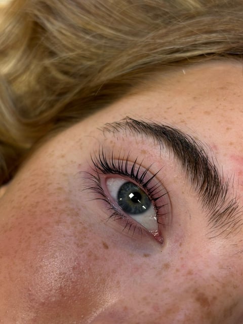 Close-up of a womans eye with blue iris, thick black eyelashes, and defined dark eyebrow